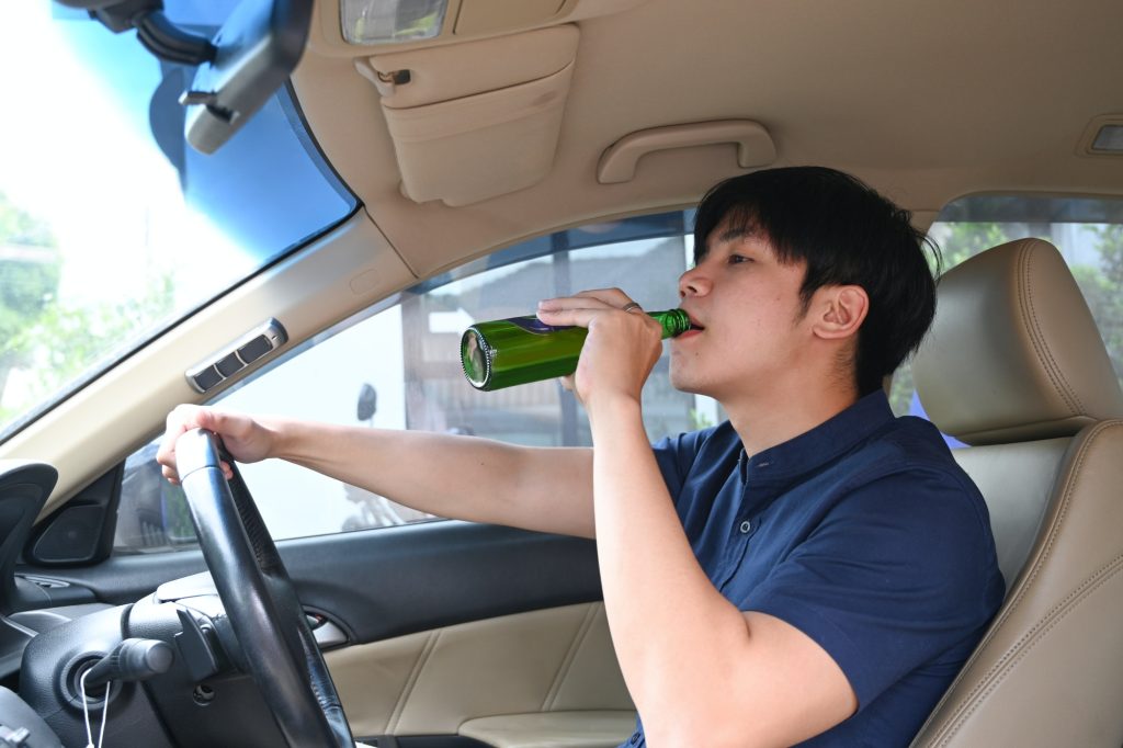 Driving under the influence. Young man drinking beer while driving a car.